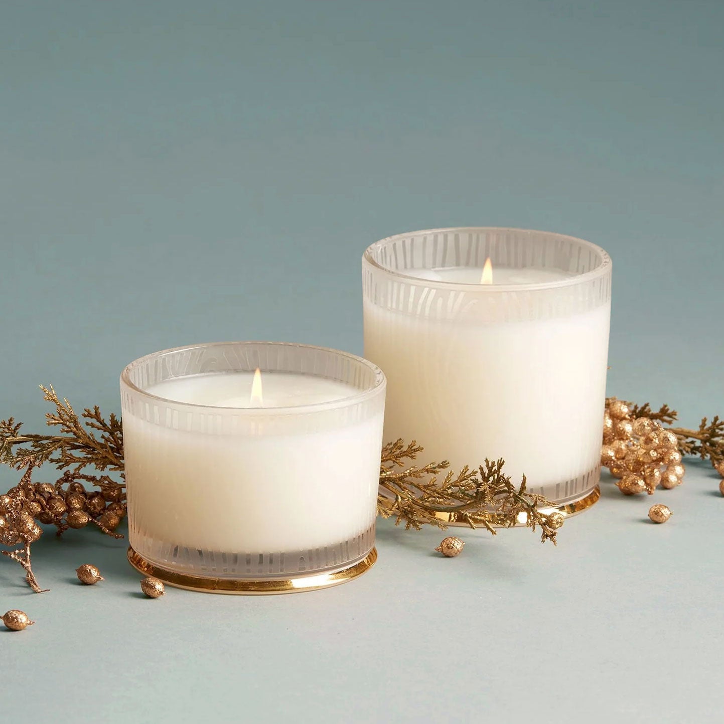 On a blue background is two frosted glass jar candles in different sizes. 