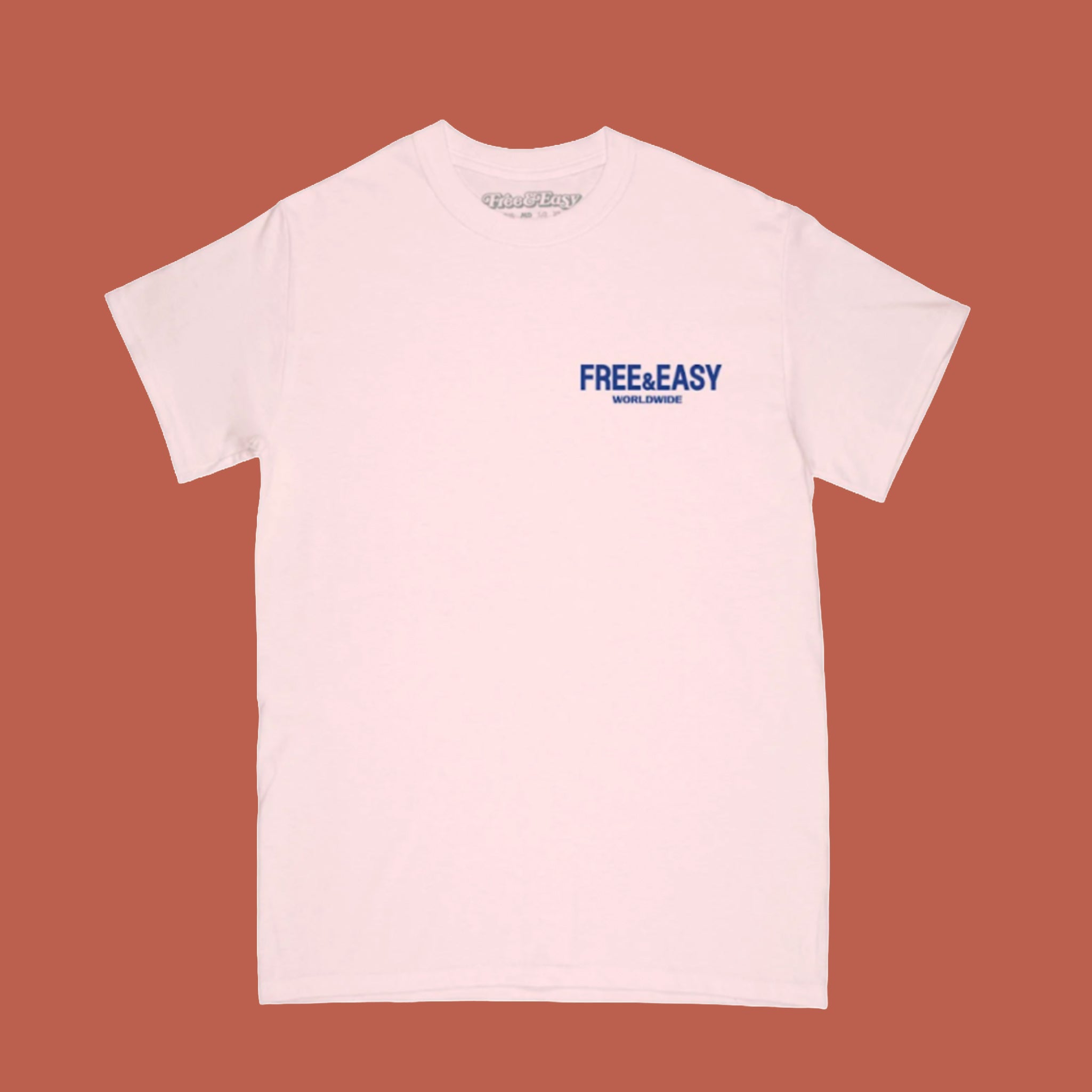 Light pink short-sleeve T-shirt with small blue “Free & Easy Worldwide” logo printed on the left chest, shown against a terracotta background.
