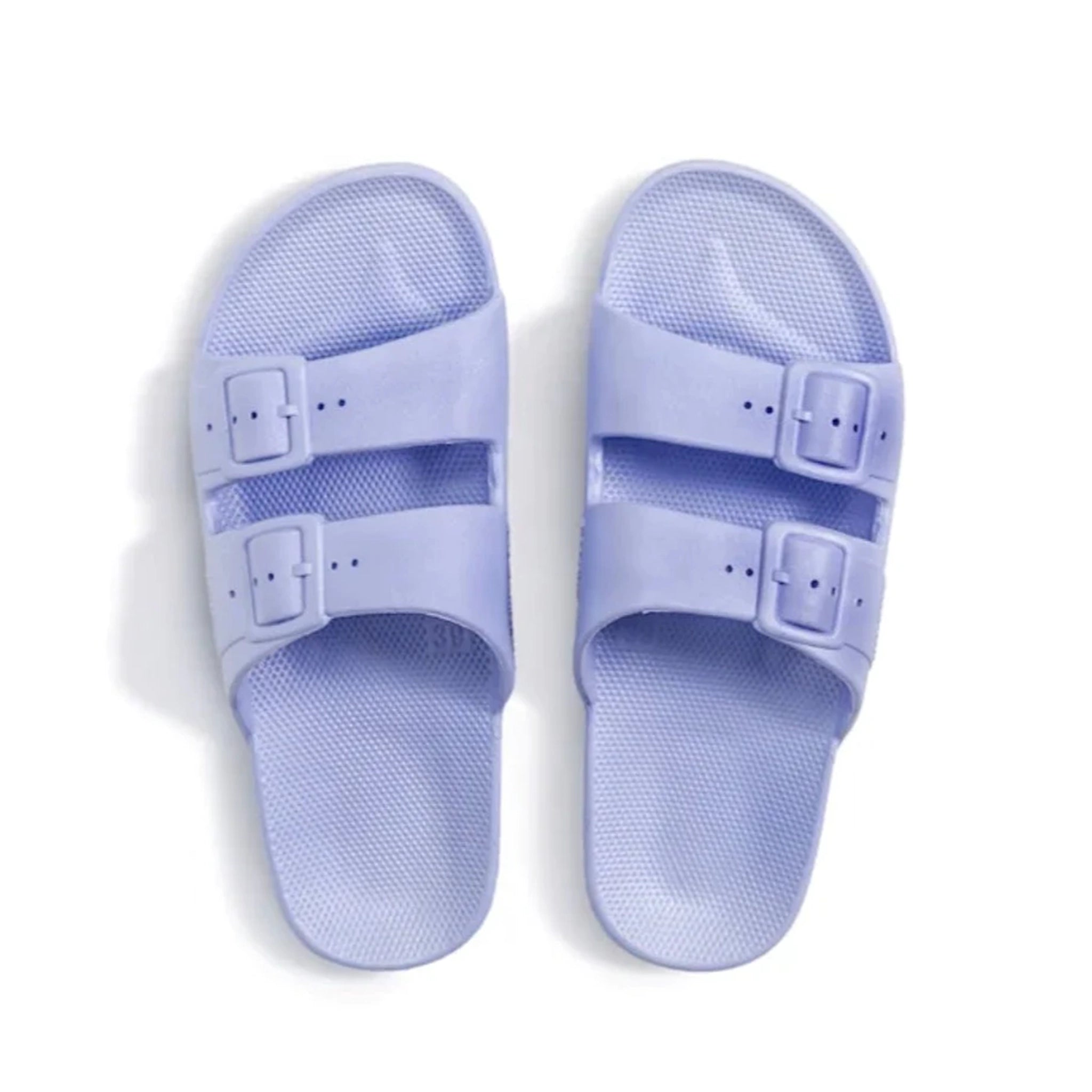 On a white background is a pair of light lavender cloud slides with two buckle straps. 