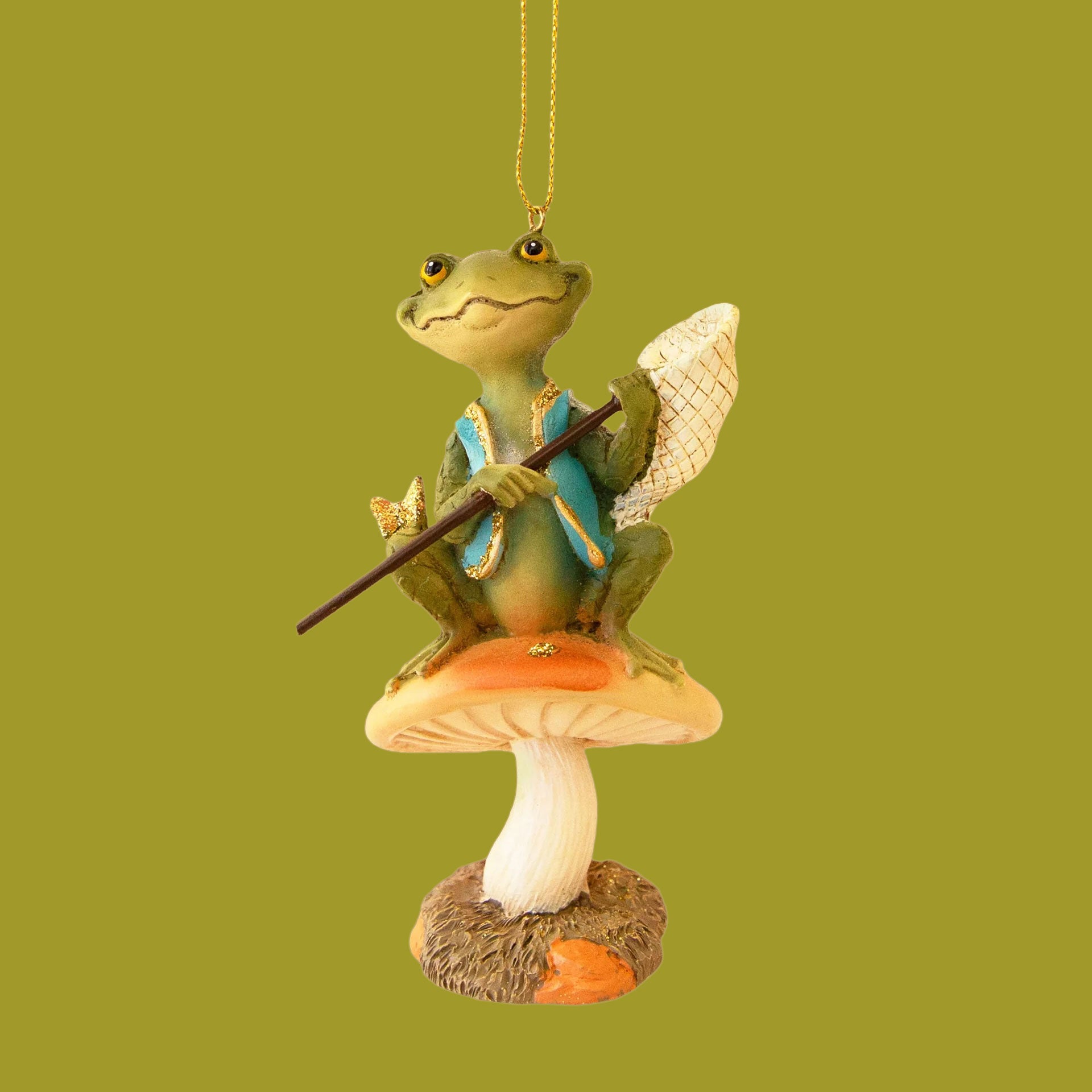 Ornament of a green frog with a teal vest on, sitting on top of an orange mushroom. The frog has a net in his hands and a gold butterfly on his knee. 