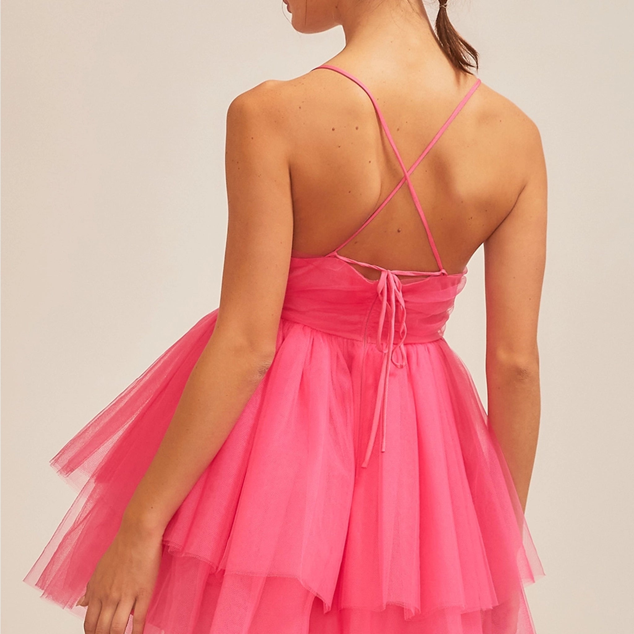 On a neutral background is a model wearing a hot pink tulle mini dress with a sweetheart neckline and thin straps.