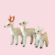 On a peachy background is three different sized mint green furry reindeer ornaments. 