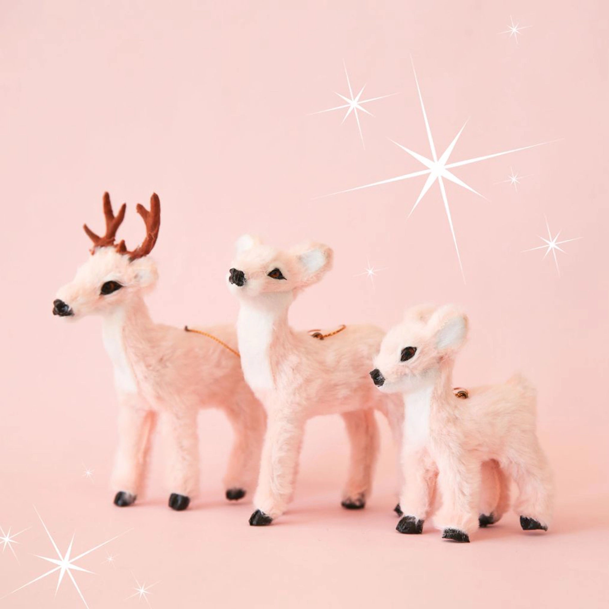 On a pink background is three different sized fur reindeer ornaments. 