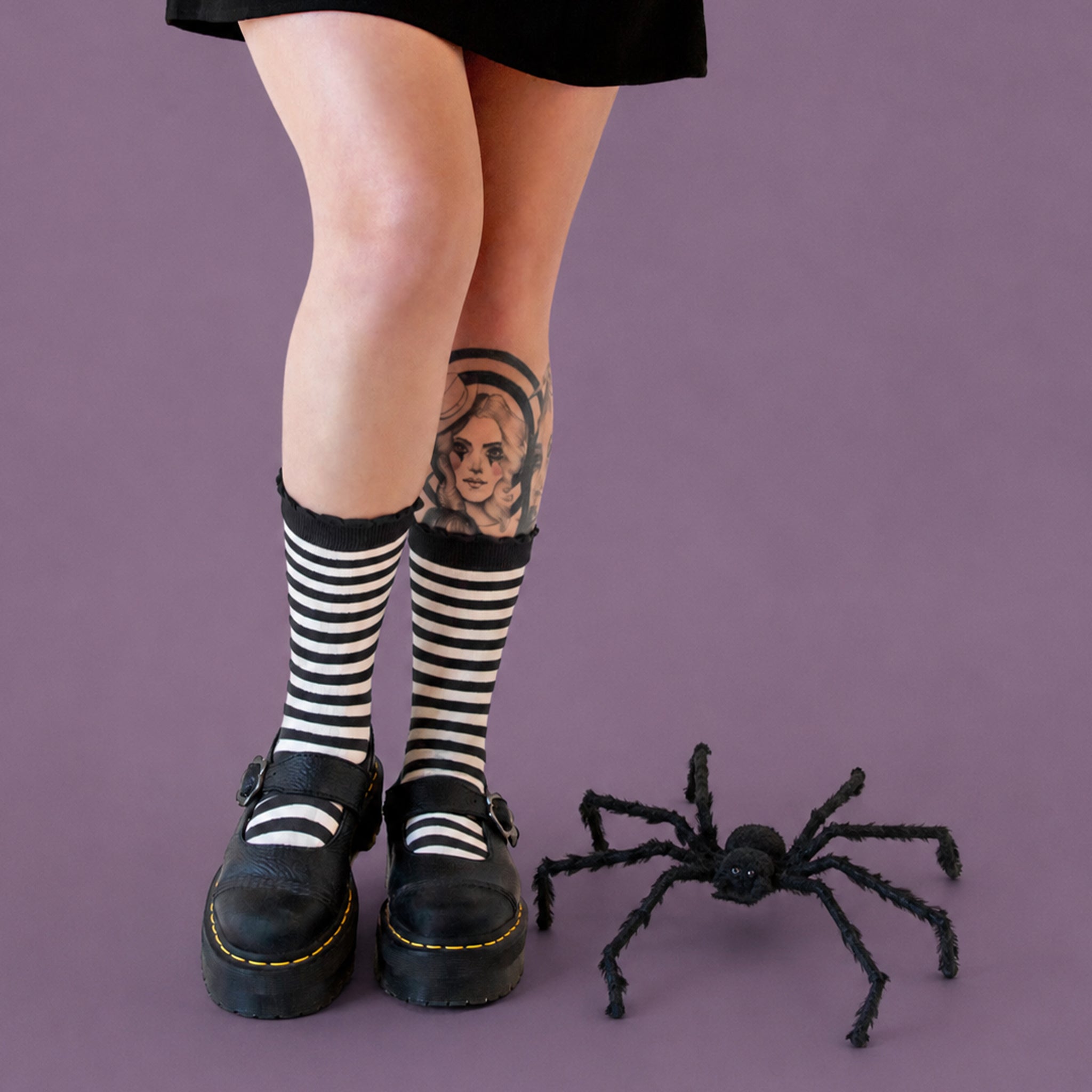 A black fuzzy spider decoration placed on a solid light purple background.
