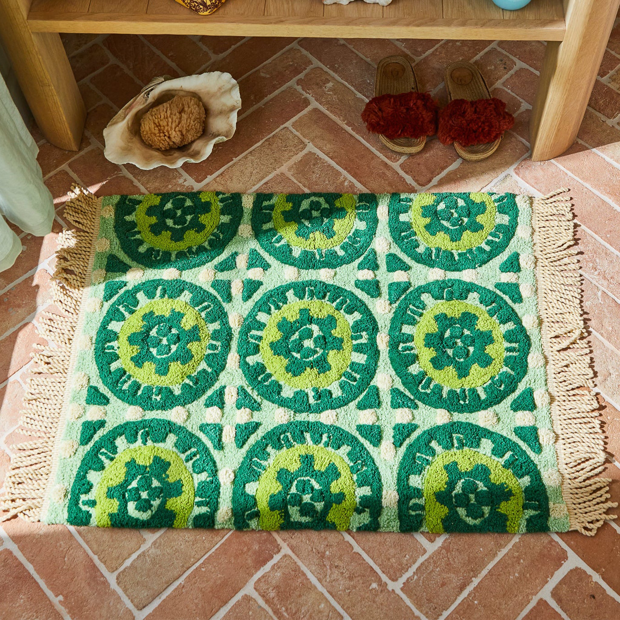 A green patterned bath mat with fringe edges. 