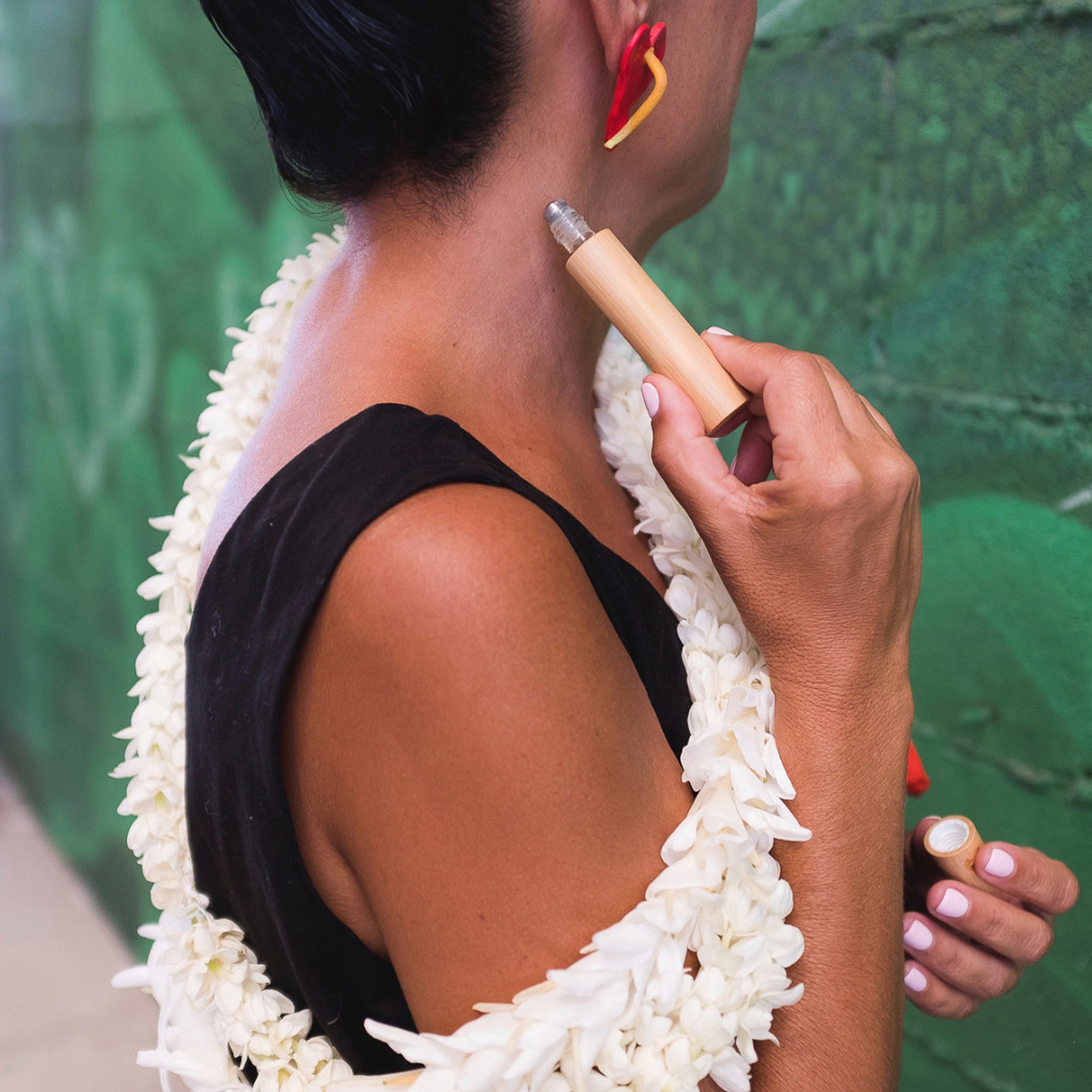 A woman putting on a roller of perfume behind her neck wearing a white floral lei.