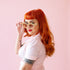 On a pink background is a model wearing the gemma sunglasses in the shade amber. 