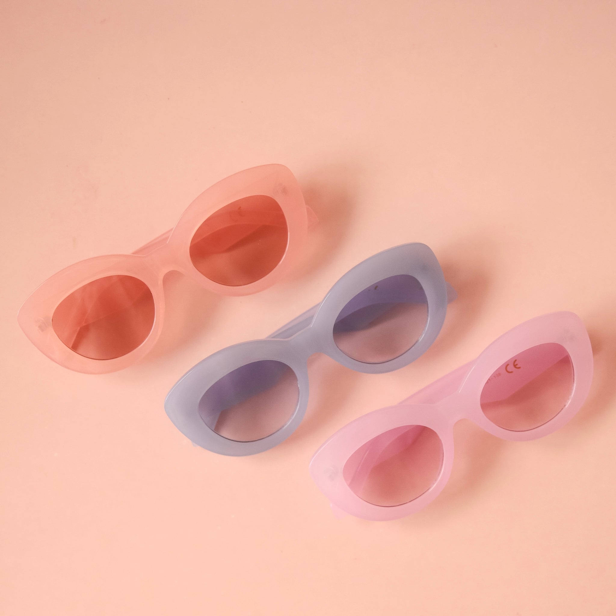 On a peachy background is a group photo of three of the different color options for the Gemma Sunglass frame shape. 