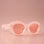 On a light peachy background is a pink pair of sunglasses with a rounded shape and a slight cateye at the corner along with a peachy lens. 