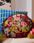 A maroon and multi colored floral round pillow with a fringe edge. 