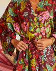 Brick red robe with colorful floral print is shown on a model. 