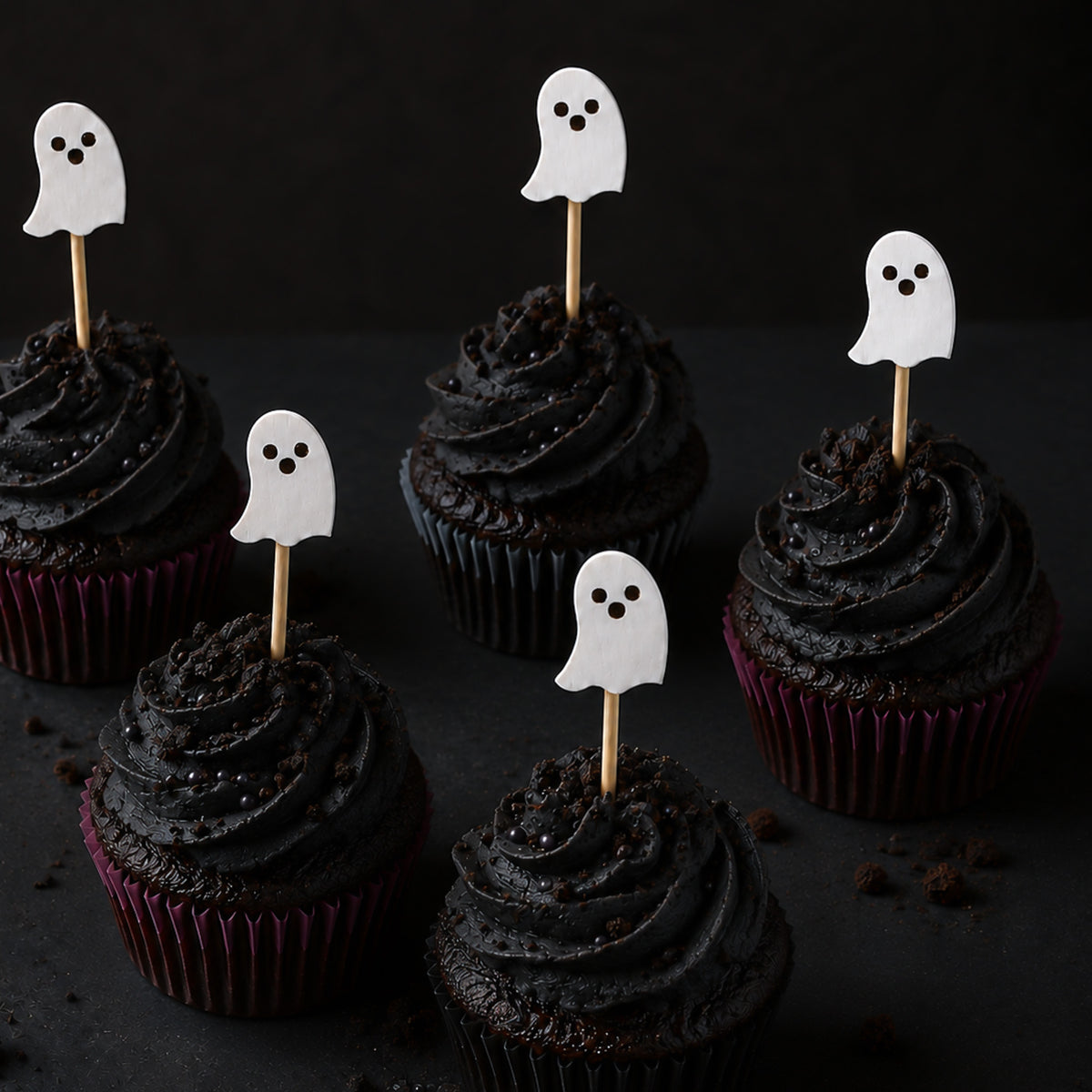 Chocolate cupcakes with black frosting and sprinkle with whit ghost toothpicks inserted in them.