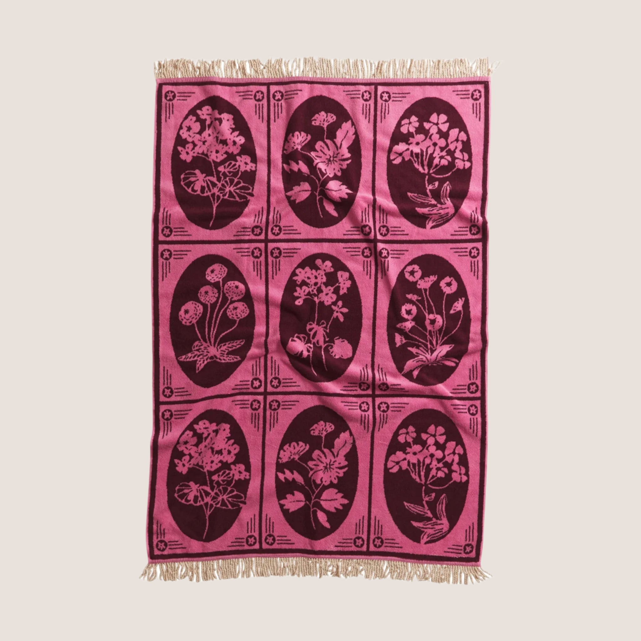 A pink and darer pink floral designed bath towel with a tassel edge on each end. 