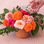 On a pink background is a bouquet of flowers in an orange fluted planter.