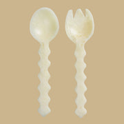 An ivory set of wavy handle salad servers. 