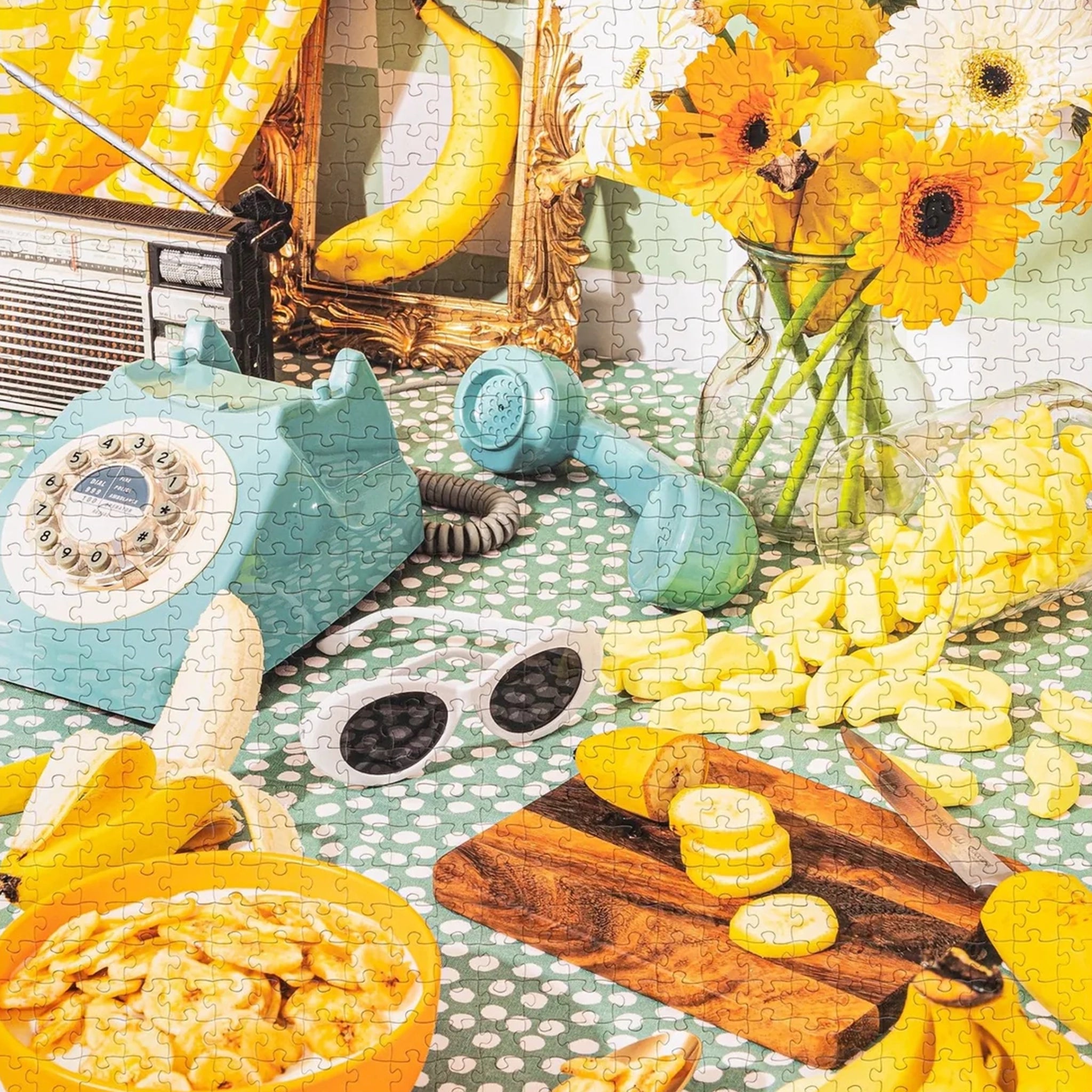 A photo of the puzzle finished that features  a retro table scape with white sunglasses lots of bananas and other yellow items. 