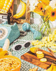 A photo of the puzzle finished that features  a retro table scape with white sunglasses lots of bananas and other yellow items. 