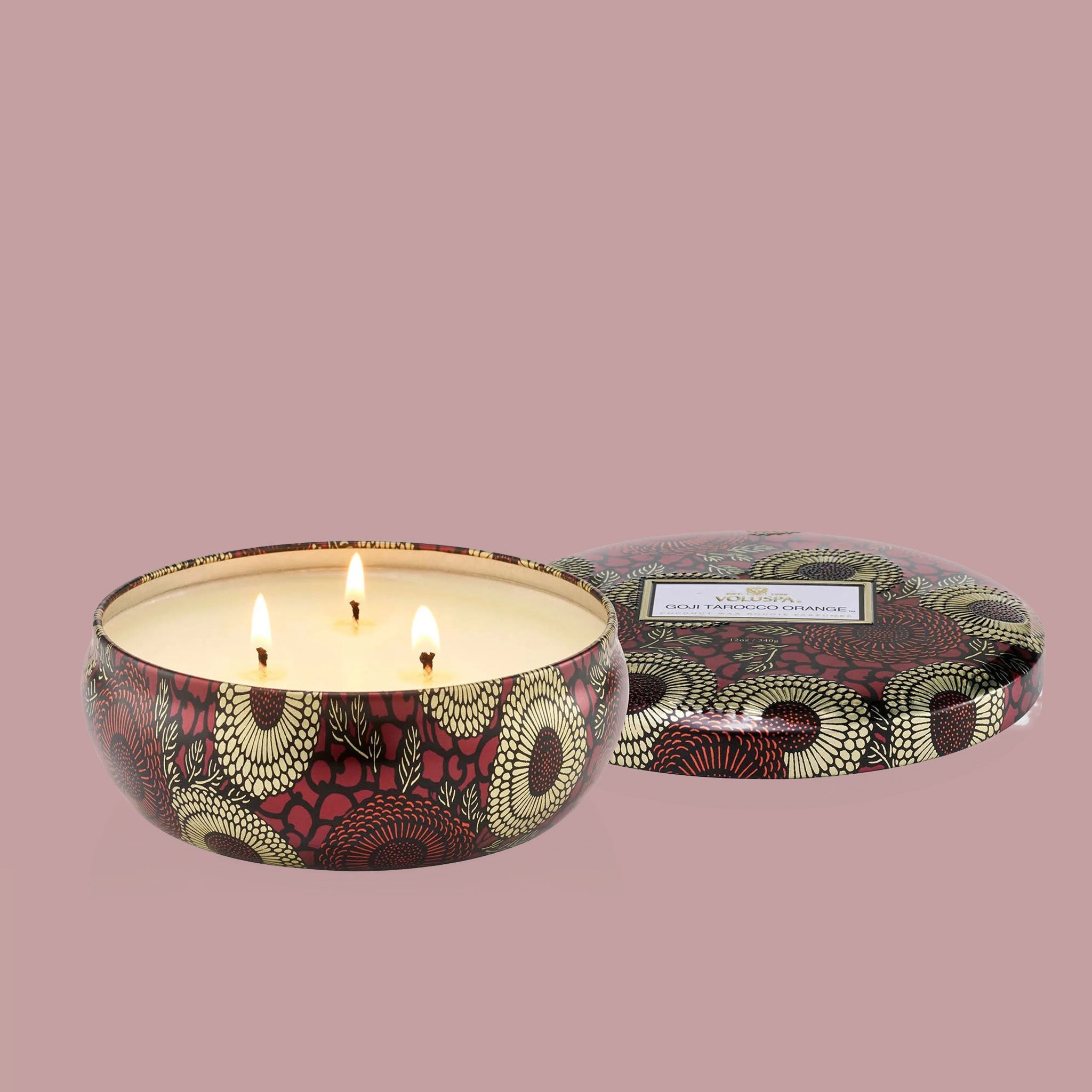 A red tin with a three wick candle inside and a label on the lid that reads, "Voluspa Goji Torocco Orange".
