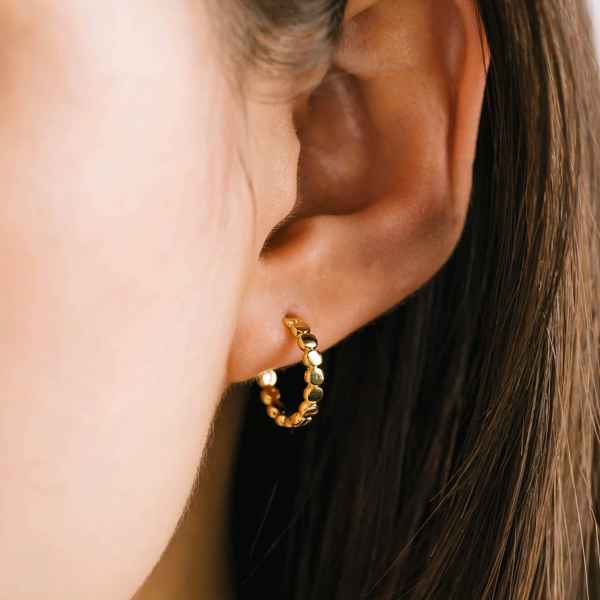 A model wearing a pair of gold hoop earrings with a dainty circle detailing on the hoops.