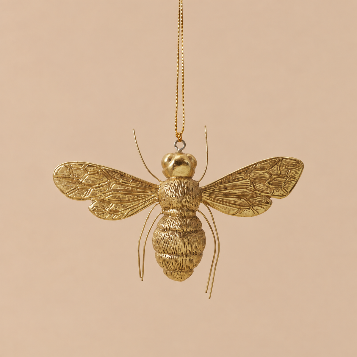 A metallic gold bumblebee hanging ornament suspended from a gold chain against a solid beige background.