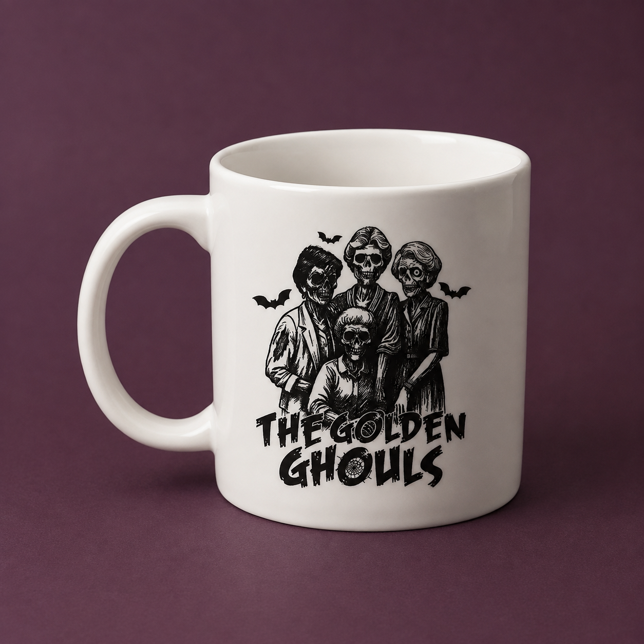 A white ceramic mug featuring a black illustration of four ghosts with the text 'THE GOLDEN GHOULS' and small bat silhouettes, set against a solid dark purple background.