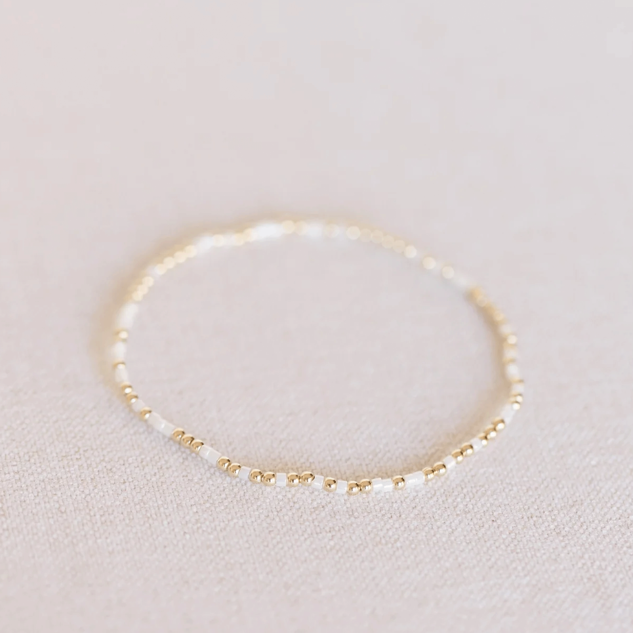 On a white background is a white and gold beaded bracelet. 