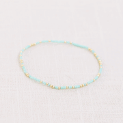 On a white background isa teal and gold bead bracelet. 