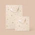 On an ivory background is two light pink gift bags with gold star details. 