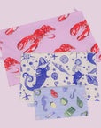 A set of three nylon packable pouches with a lobster print, a mermaid print and a sea creature print. 
