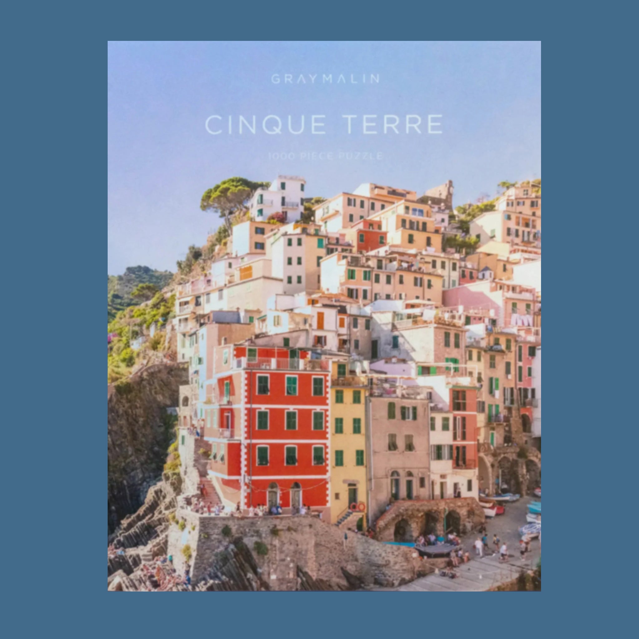 A puzzle box that looks like a book cover with a photograph of a cliffside in Cinque Terre and text that reads, 'Gray Malin Cinque Terre'. 