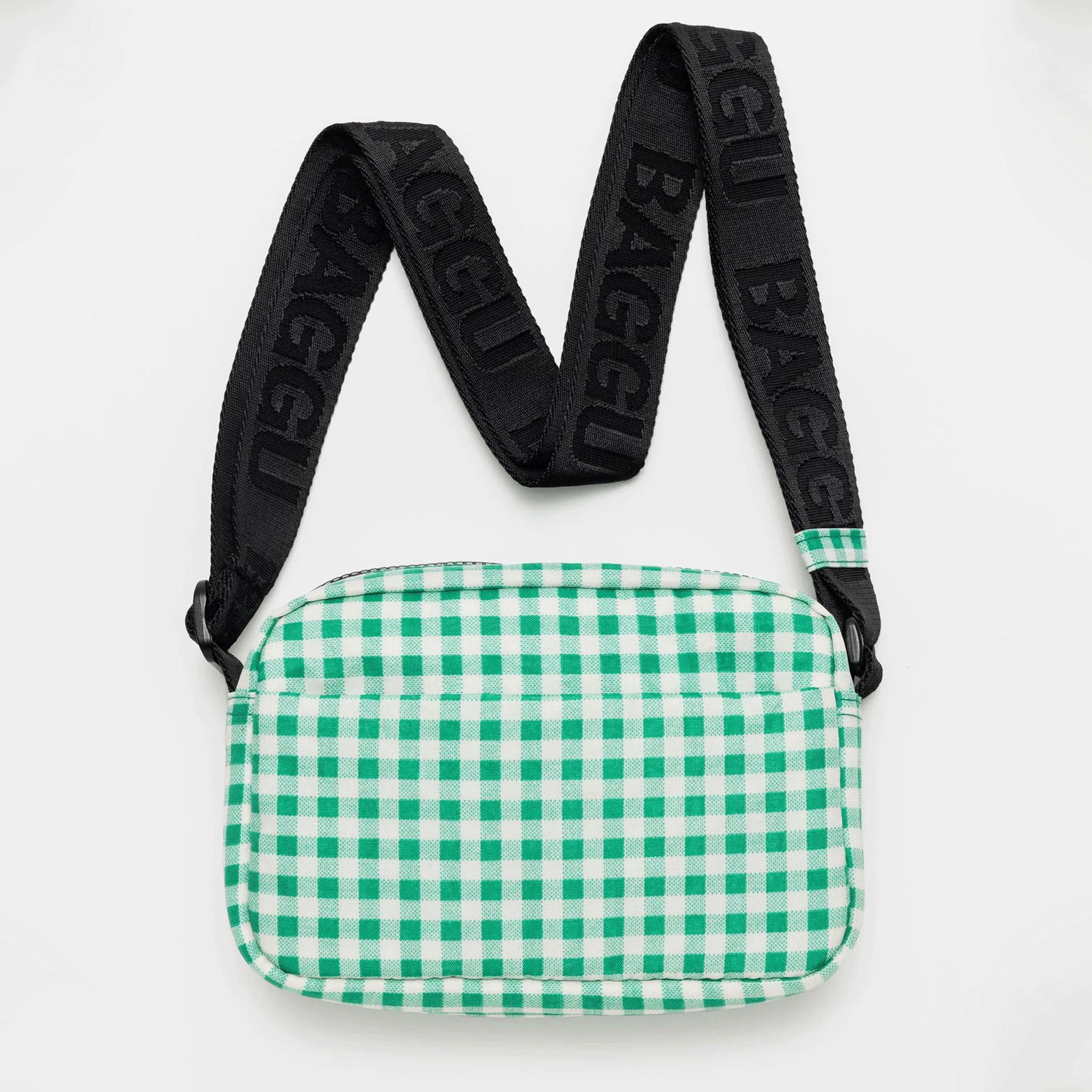 On a white background is a green and white gingham crossbody bag with a black strap. 