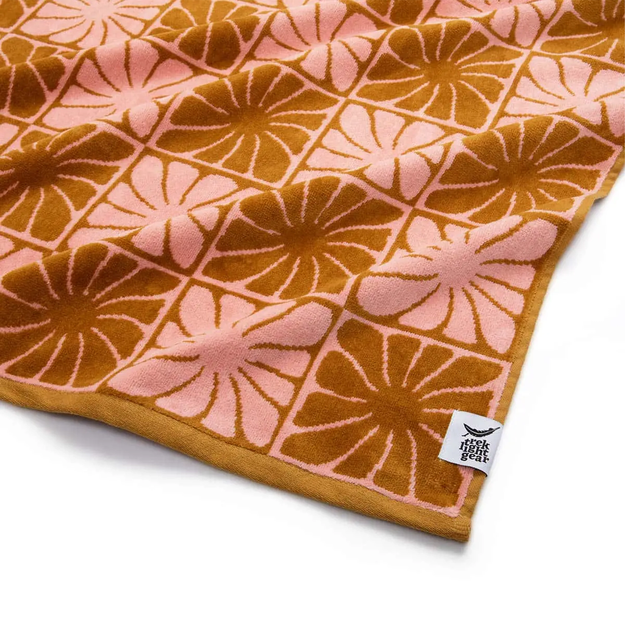 A pink and burnt orange bath/beach towel with a wavy floral checker design in each of the squares photographed here laid flat on a white background. 