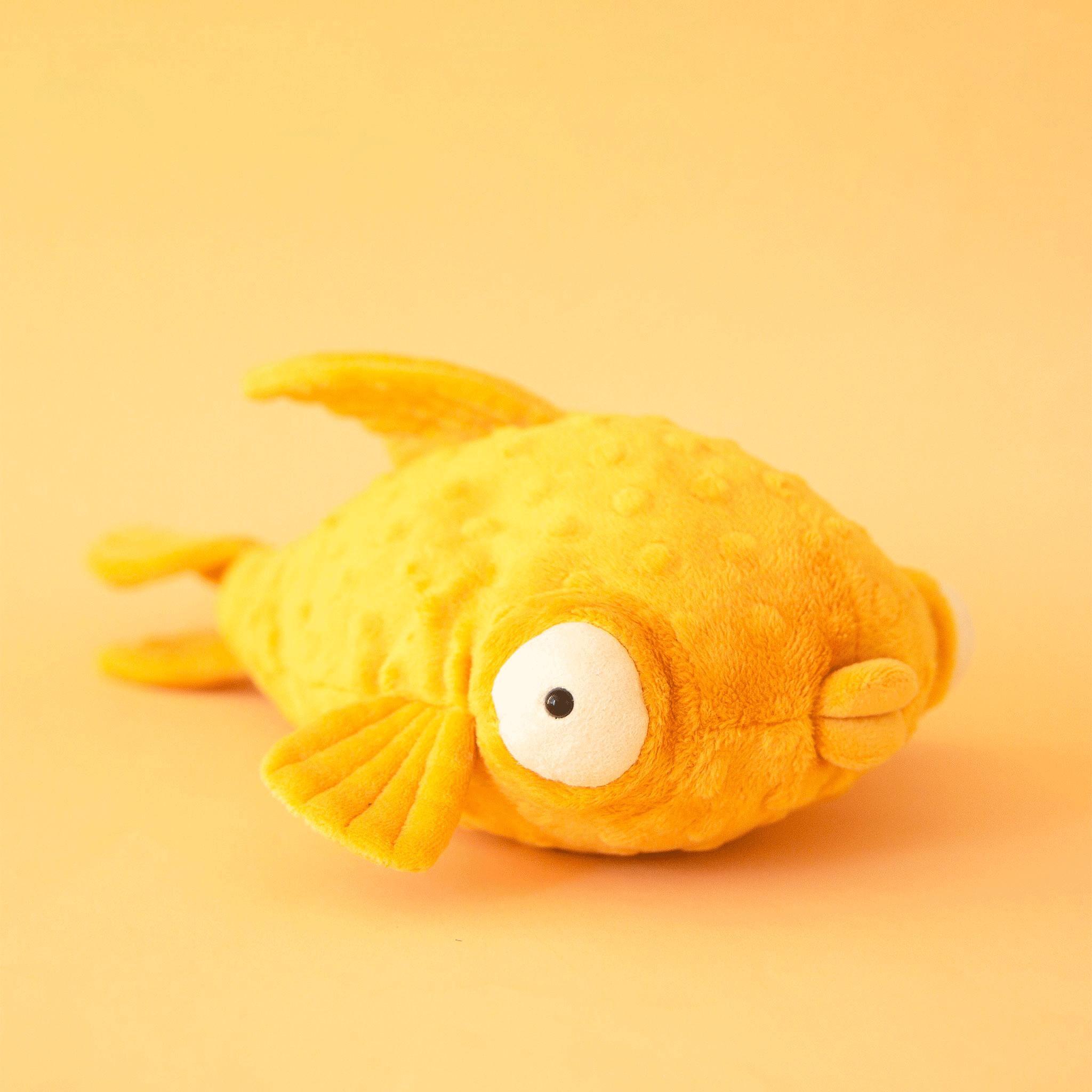 On a yellow background is a yellow stuffed toy fish with puffy eyes and lips.