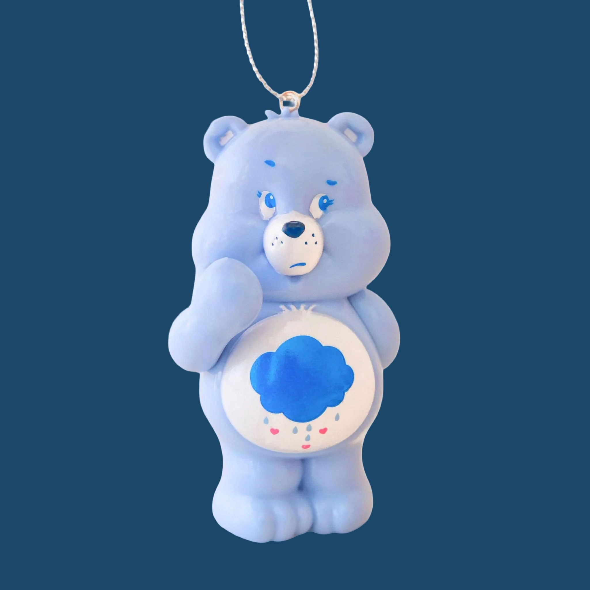 A blue care bear shaped glass ornament with a raincloud graphic on its stomach. 