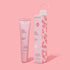 Light pink ESW Beauty ‘Guava Mango Smoothie’ lip treatment tube standing beside its matching candy-cane patterned box with a loop handle on a pastel pink background.