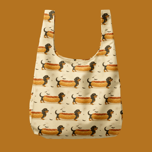 A reusable shopping bag with a repeating pattern of dachshund dogs in hot dogs on a cream background, shown against a solid brown background.