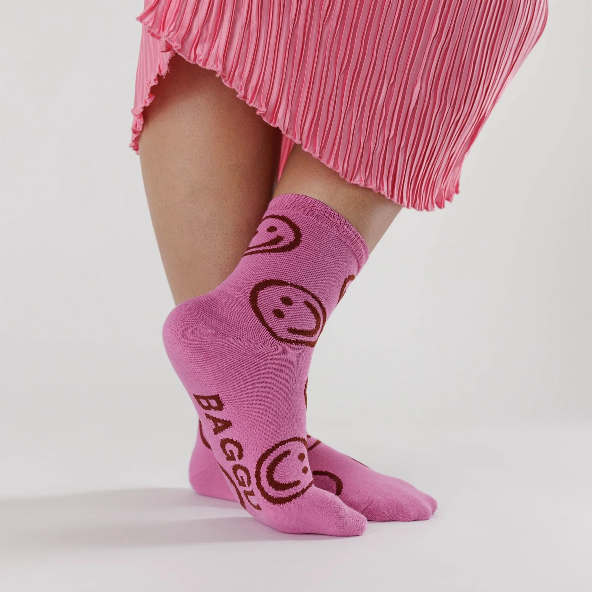On a white background is a pair of hot pink socks with a smiley face print all over. 