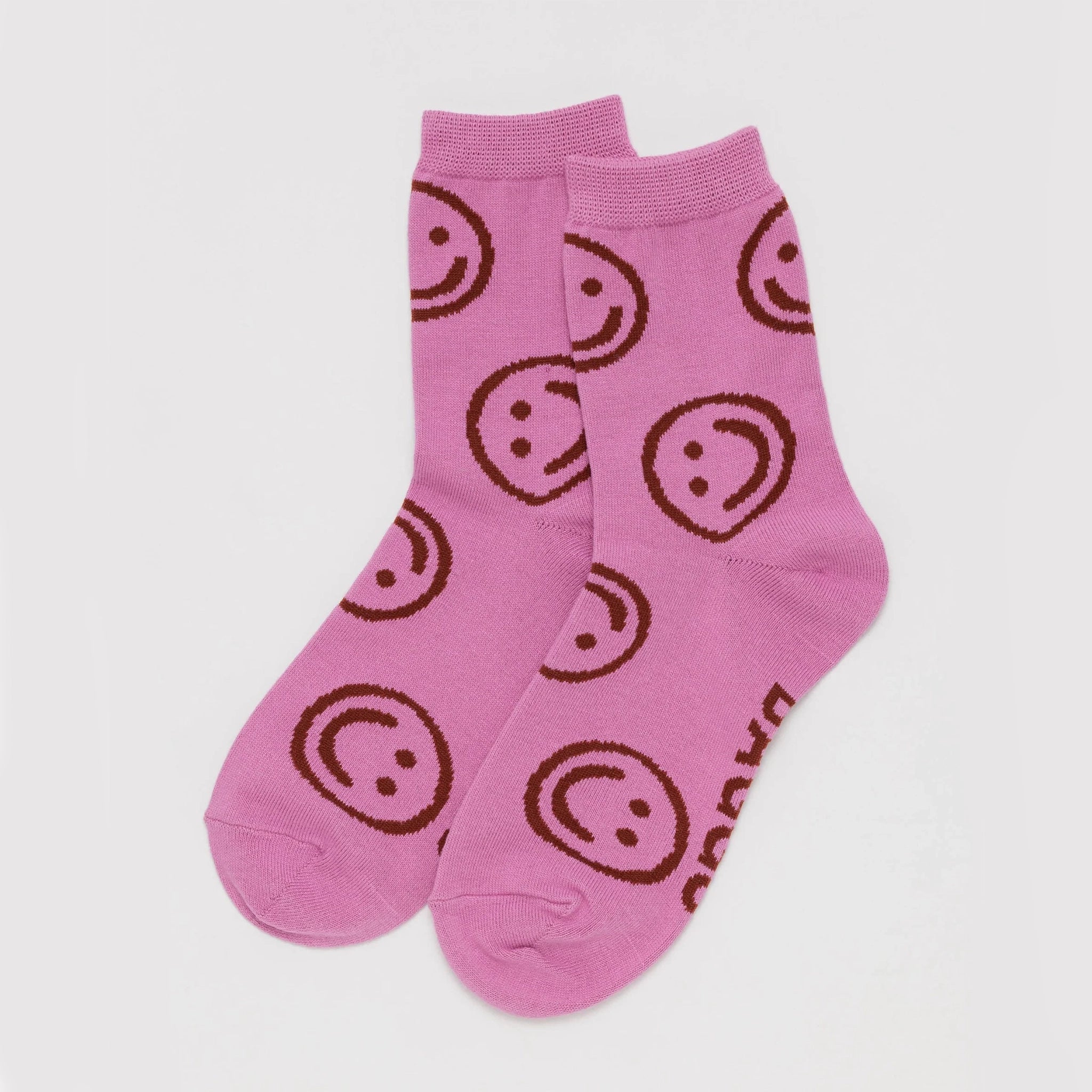xOn a white background is a pair of hot pink socks with a smiley face print all over.