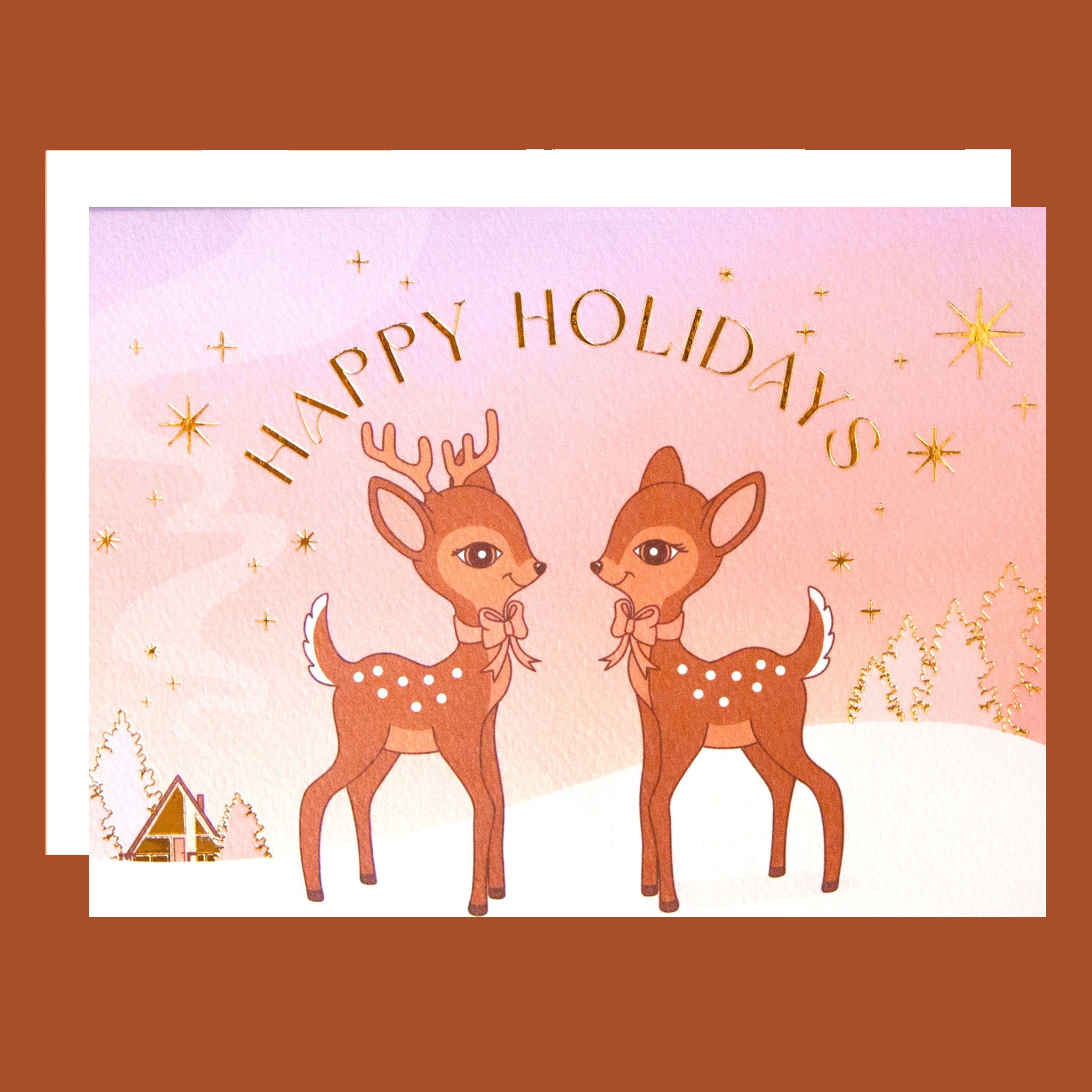 On an orange background is a greeting card with two brown retro deer graphics along with gold foiled details and text that read, "Happy Holidays".