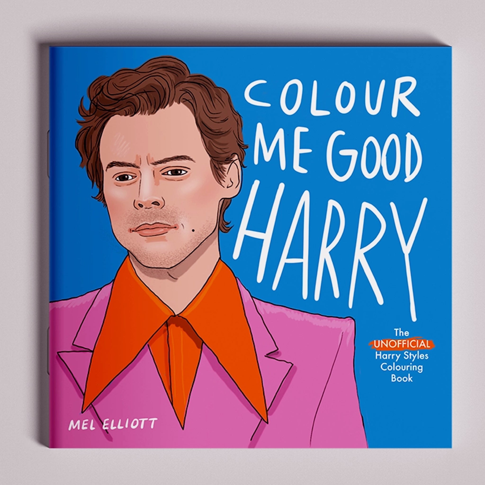 On a grey background is a blue coloring book cover with an illustration of Harry Styles and text that reads, &quot;Colour Me Good Harry&quot;. 