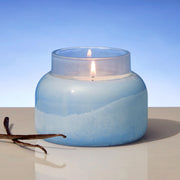 Blue glass candle with vanilla bean on a light background