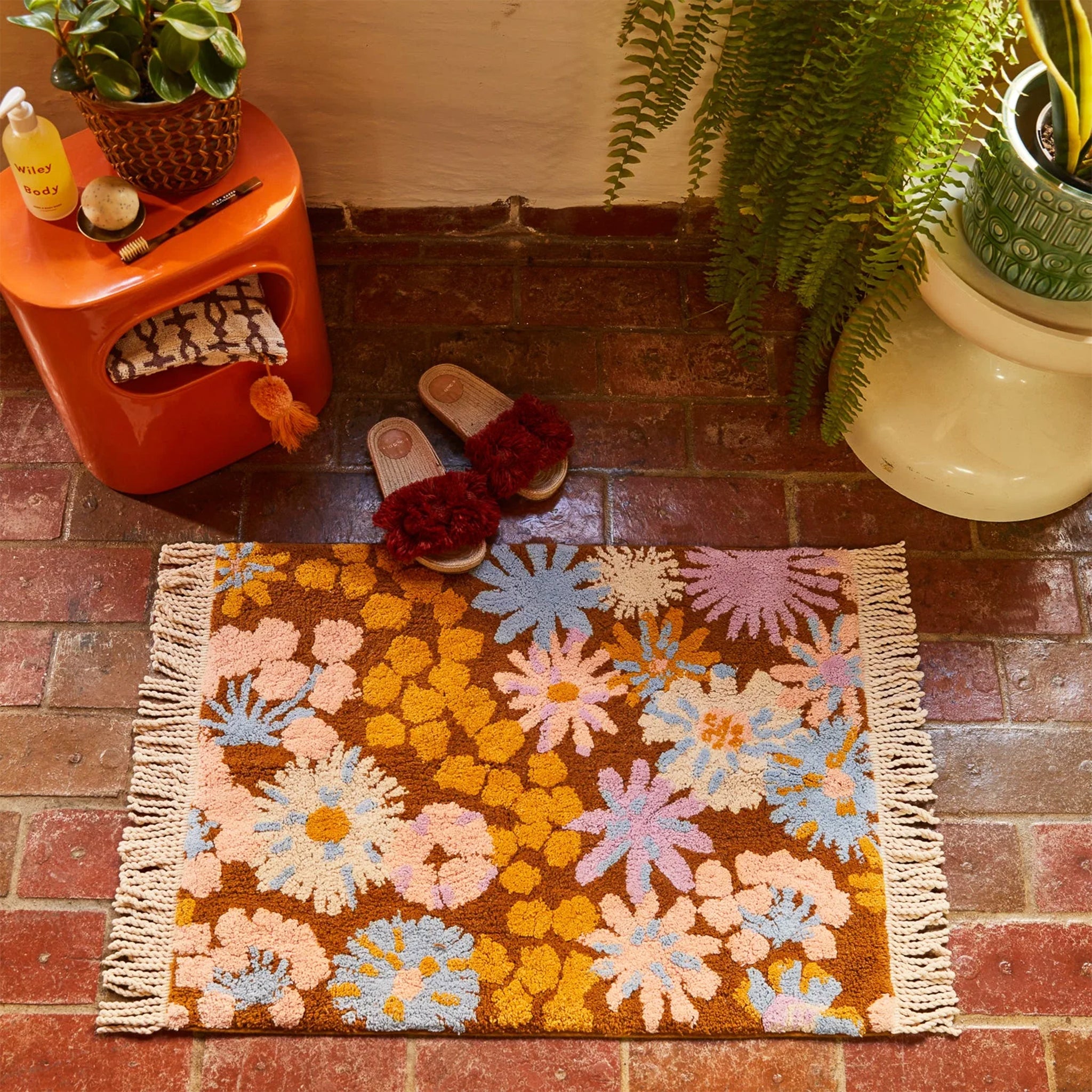 A floral, burnt orange, blue and pink bath mat with fringe edges.