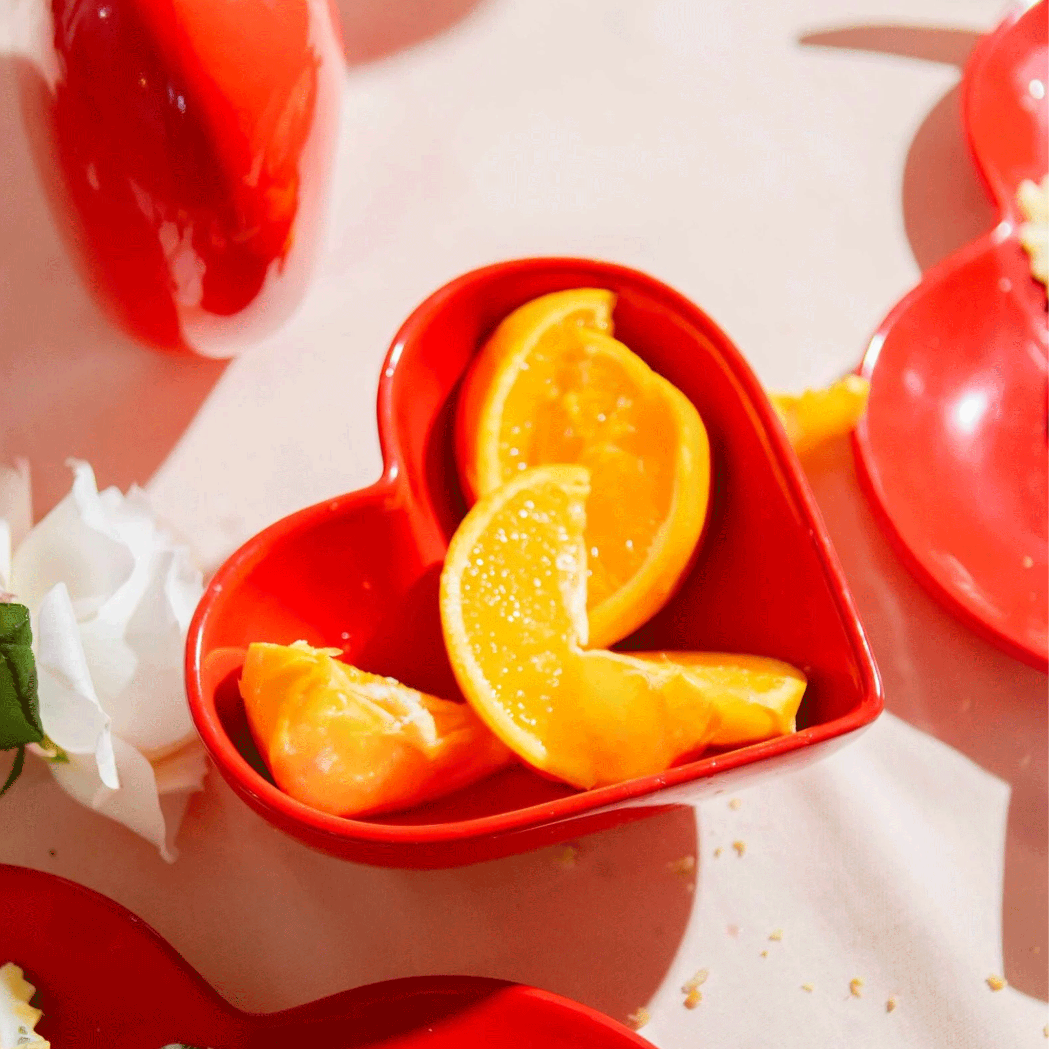 A red ceramic heart shaped bowl holding sliced oranges. 