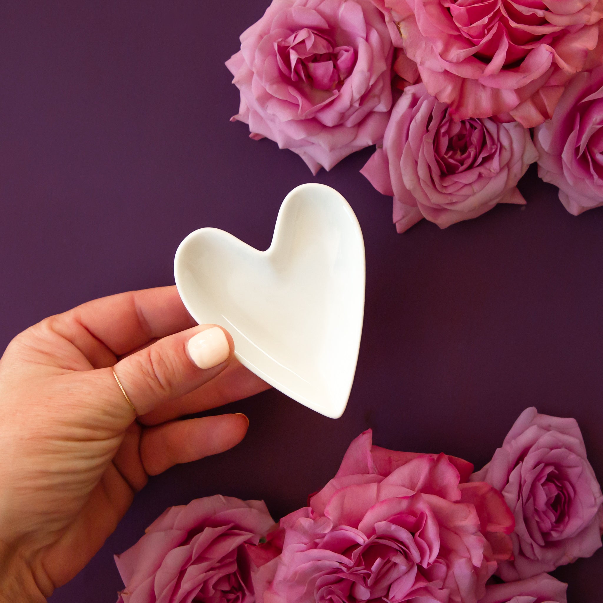 A white, ceramic, heart shaped trinket dish sits on a hot pink background