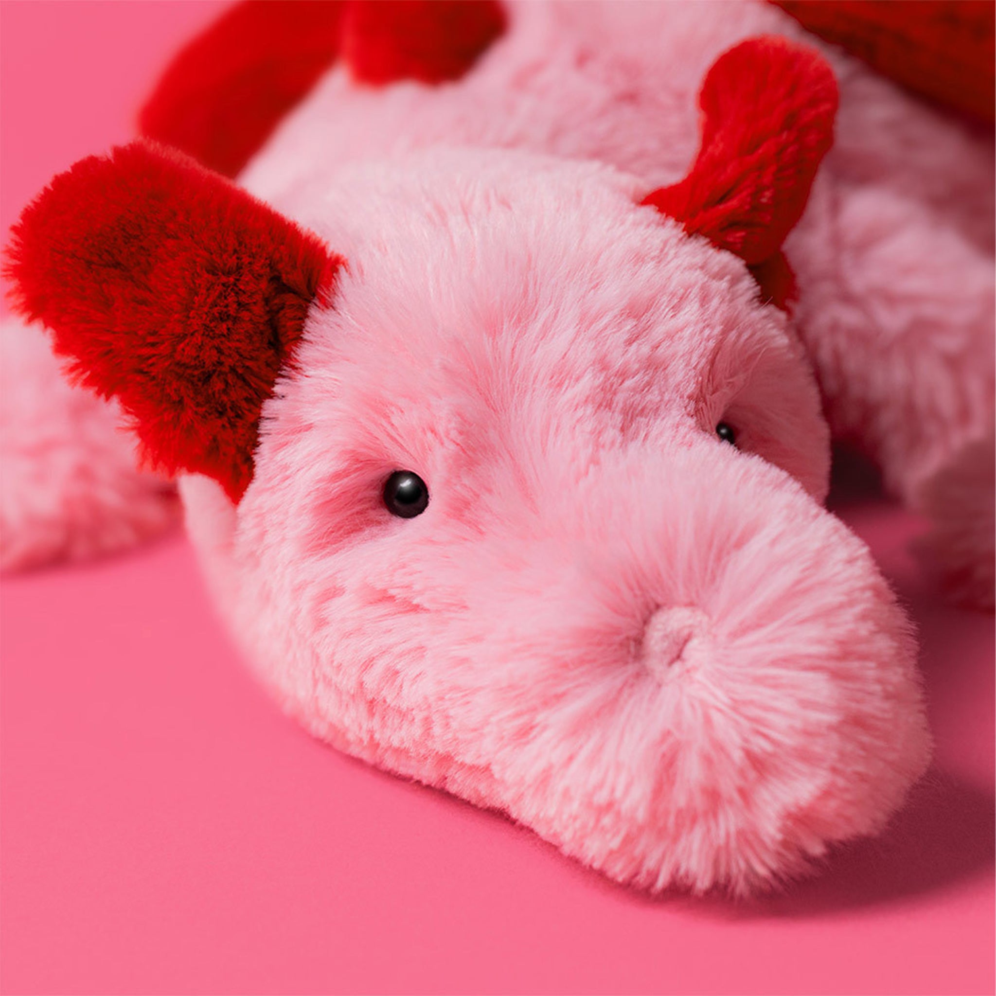 A pink and red dragon shaped stuffed animal. 