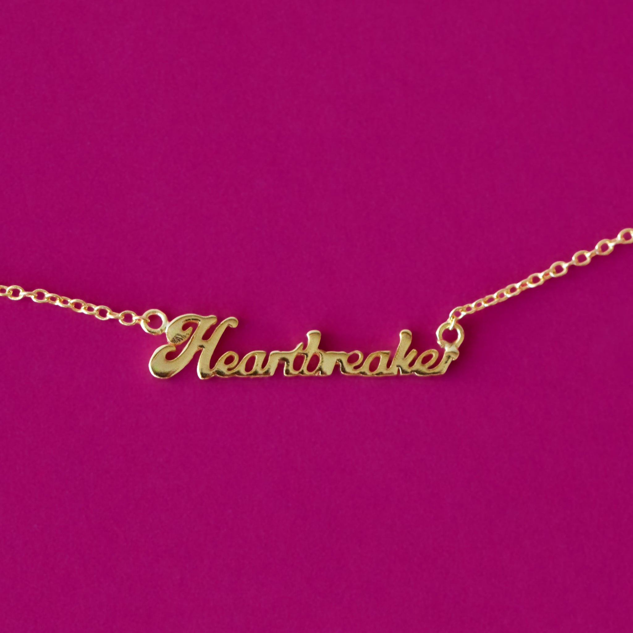 A gold name plate style necklace that reads, "Heartbreaker". 