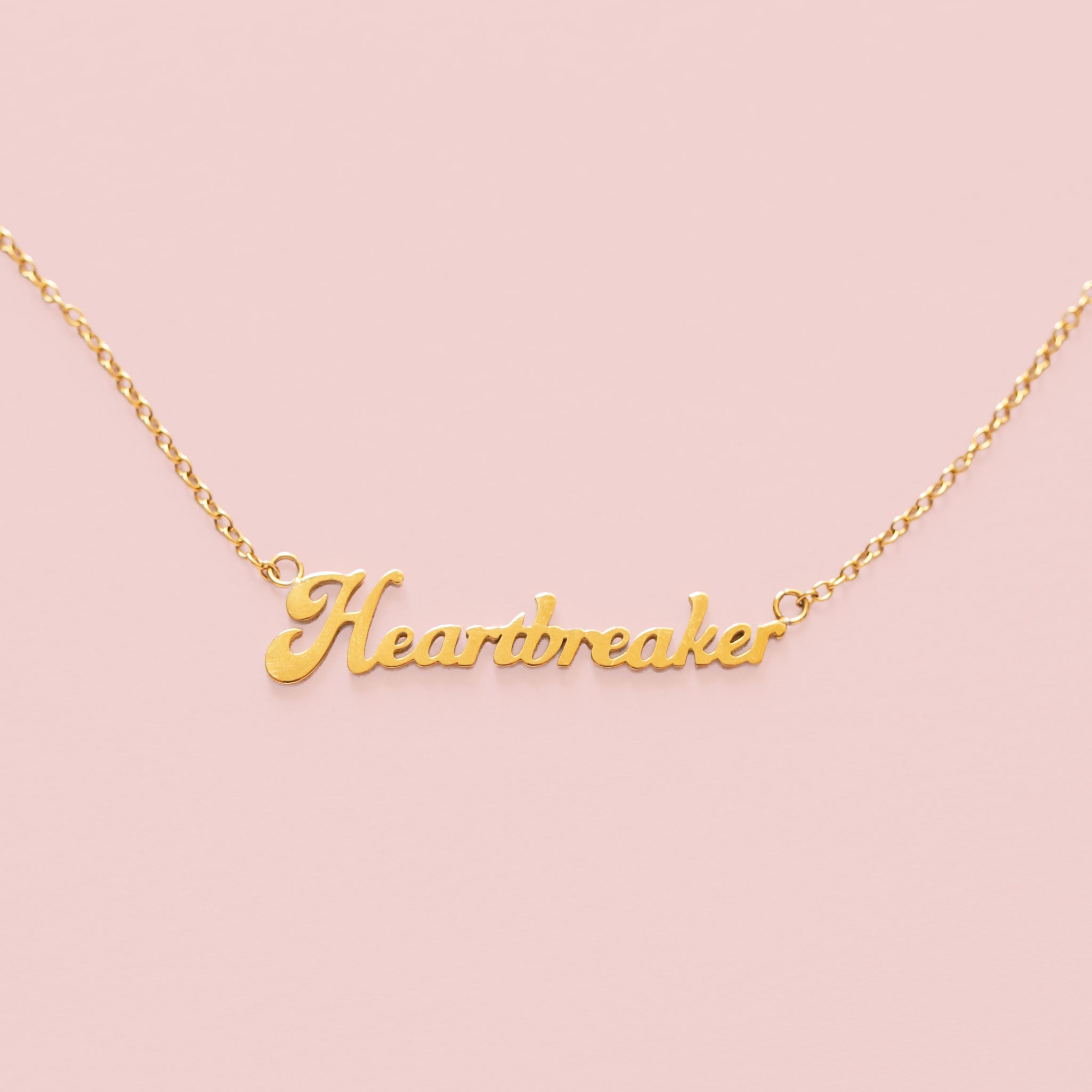 A gold name plate style necklace that reads, "Heartbreaker". 