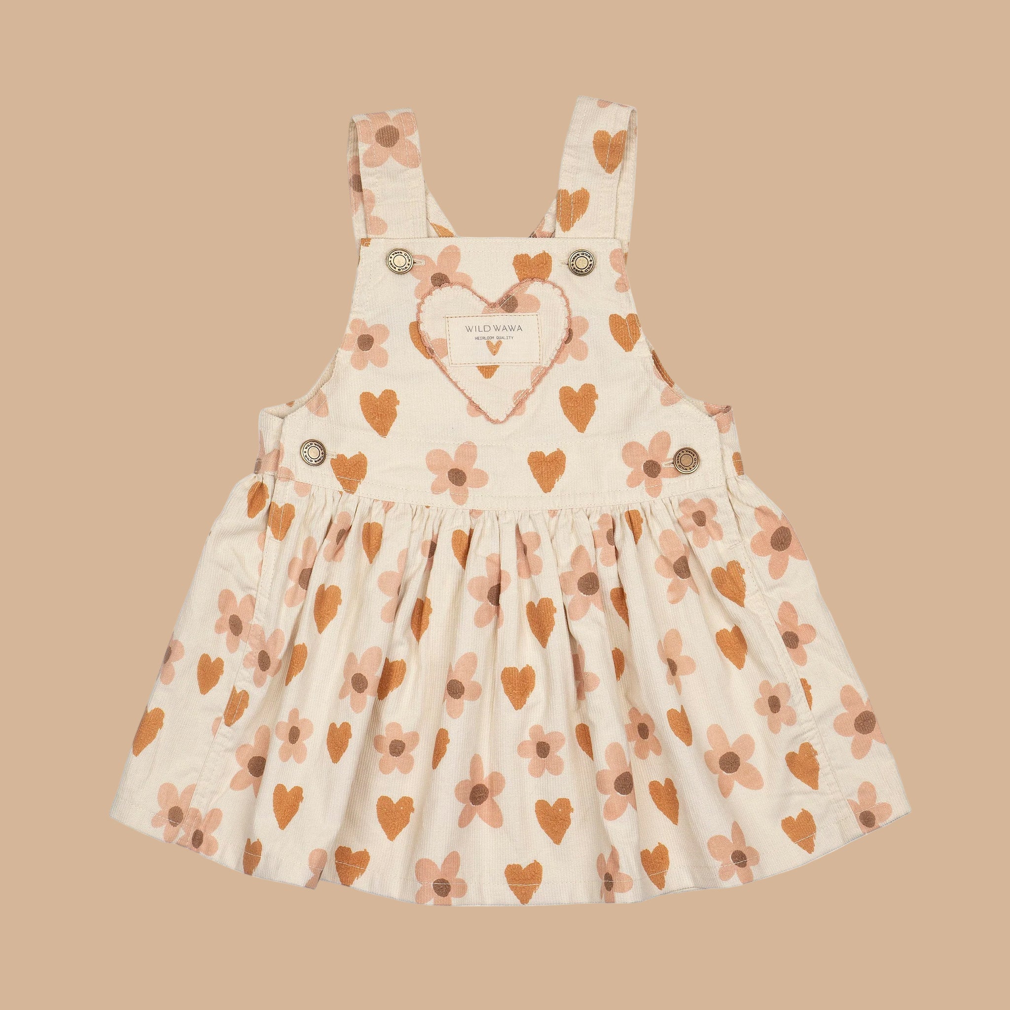 A cream colored overall dress with a burnt orange and pink heart and floral pattern. 