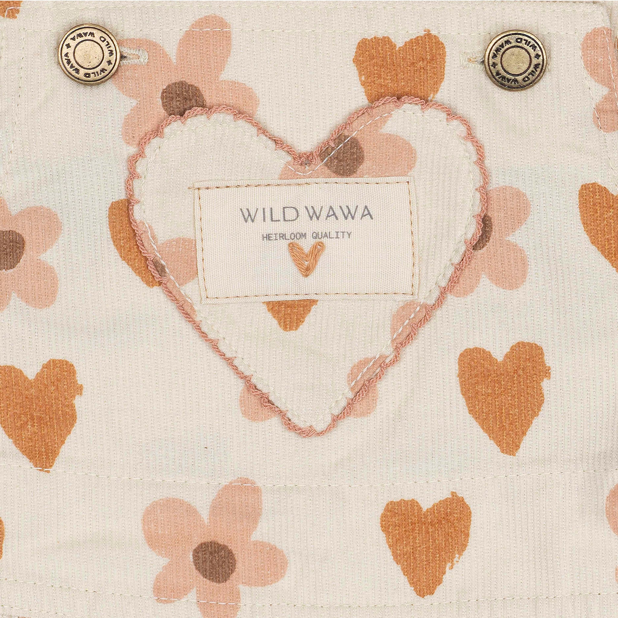 A cream colored overall dress with a burnt orange and pink heart and floral pattern. 