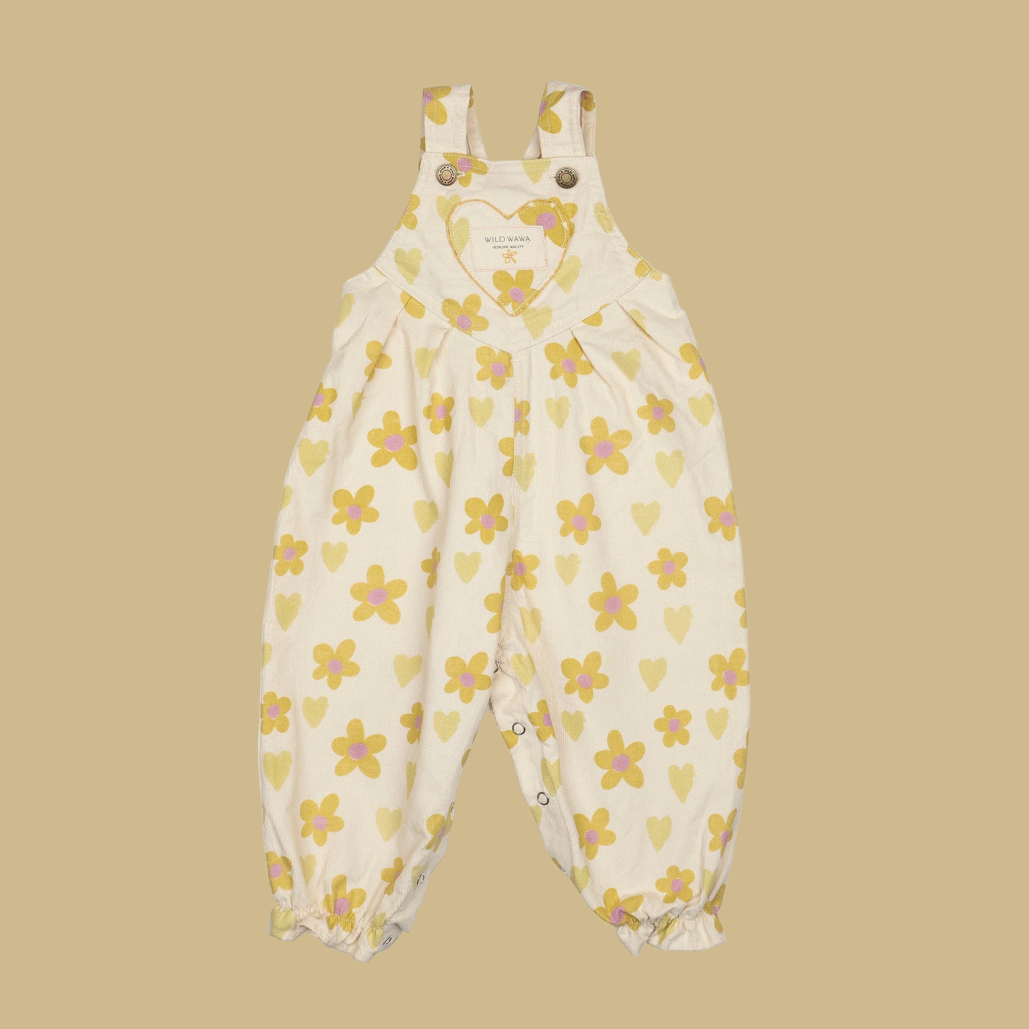 A cream colored pair of overalls with a yellow and pink floral and heart pattern. 